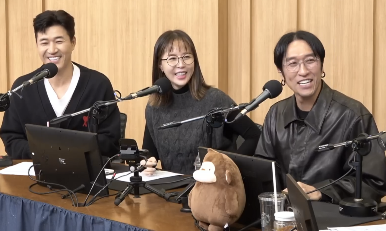 코요태 멤버 세 사람이 라디오 스튜디오의 마이크 앞에 나란히 앉아 웃고 있습니다.